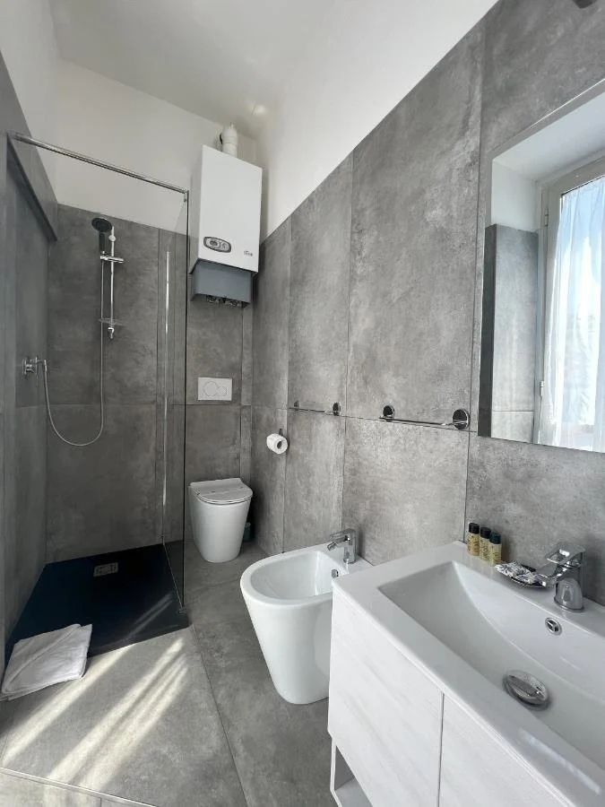Bagno luminoso con rivestimento grigio, doccia a vetro e sanitari sospesi