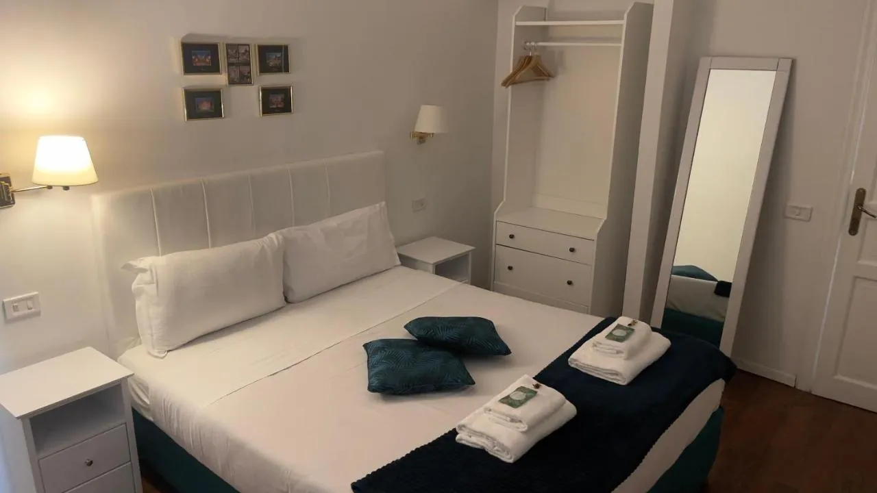 Letto matrimoniale con testiera bianca, cuscini verde petrolio e asciugamani piegati