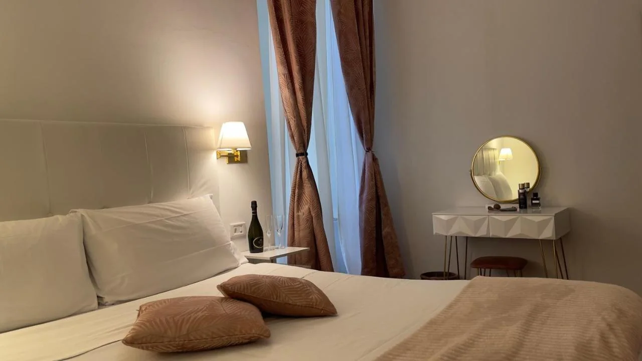 Camera rosa cipria con tende a motivo di foglie, specchio rotondo dorato e letto matrimoniale