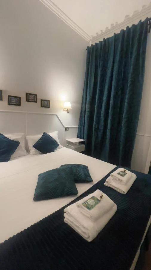 Cuscini verde petrolio e asciugamani piegati su un copriletto blu notte, accanto a una tenda blu petrolio